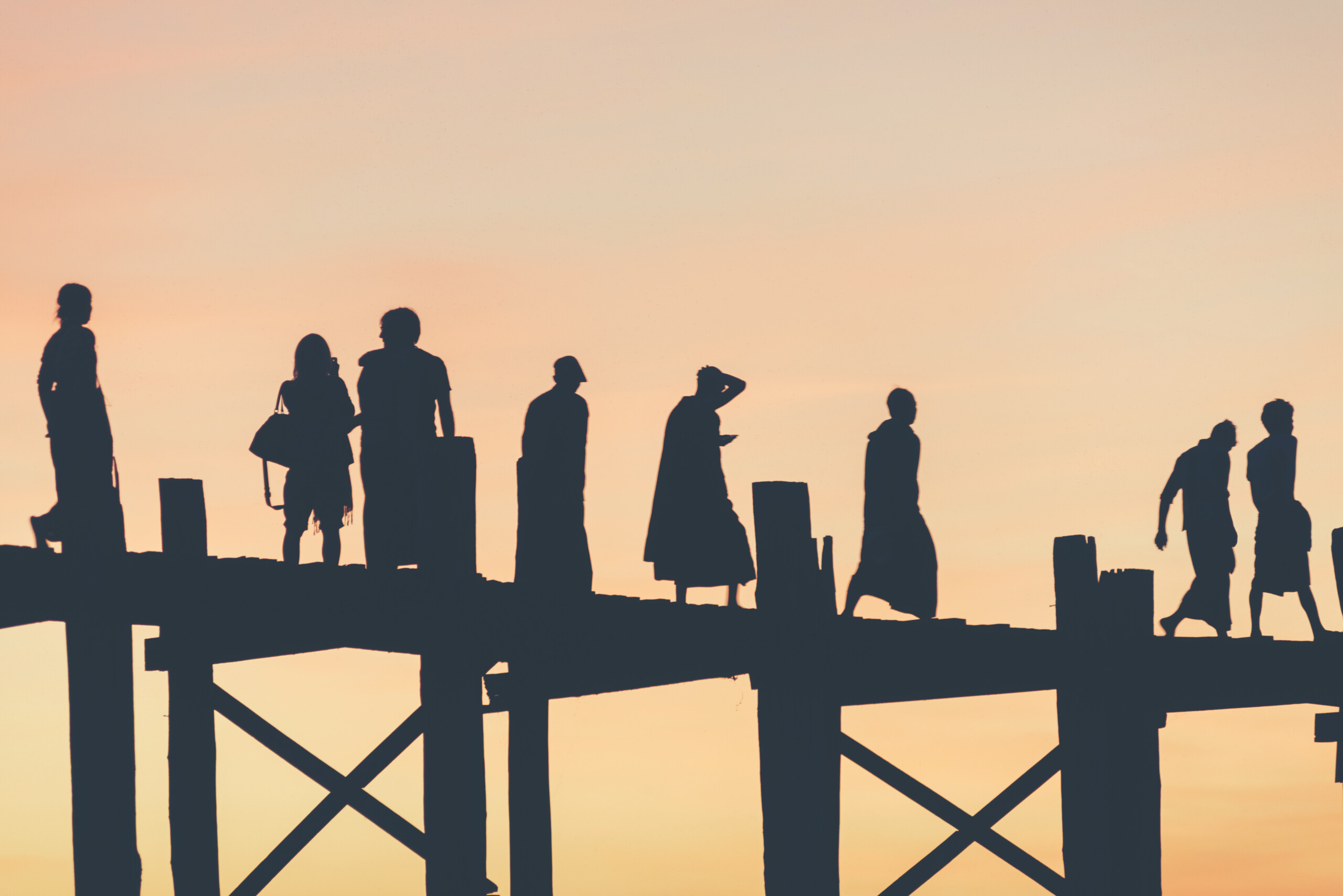 Des personnes traversent une passerelle au coucher du soleil